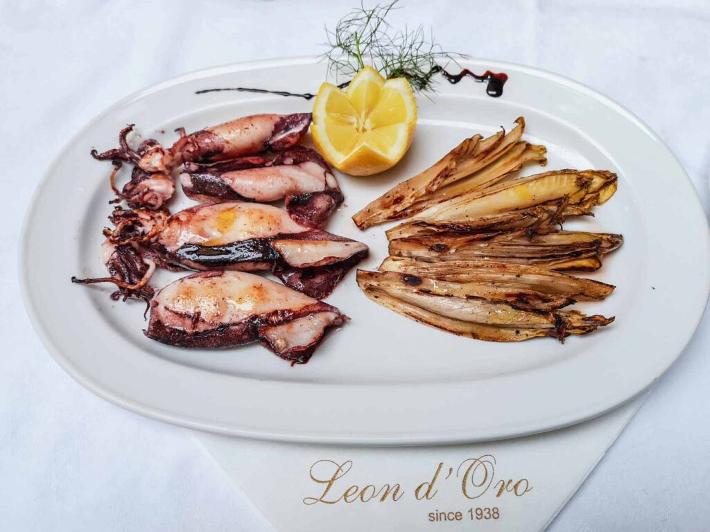 Restauranttipp für Riva del Garda am nördlichen Gardasee in Italien: Das Bild zeigt einen Teller mit Calamari und Chicorée auf einem weiß gedeckten Tisch im Restaurant Leon d'Oro in Riva del Garda