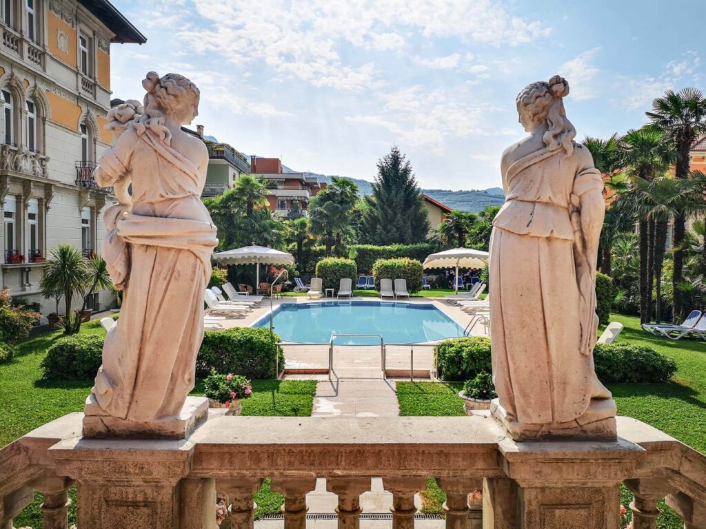 Riva del Garda am nördlichen Gardasee in Italien: Das Bild zeigt den Blick auf den Swimmingpool des Gran Hotel Liberty von der Terrasse aus. Im Vordergrund sind zwei antike römische Frauenskulpturen zu sehen