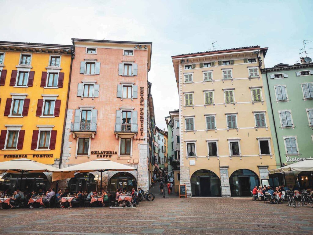 Riva del Garda am nördlichen Gardasee in Italien: Das Bild zeigt die Vorderansicht des Hotels Portici an der Piazza III Novembre mit Blick in eine verwinkelte Gasse in der Altstadt