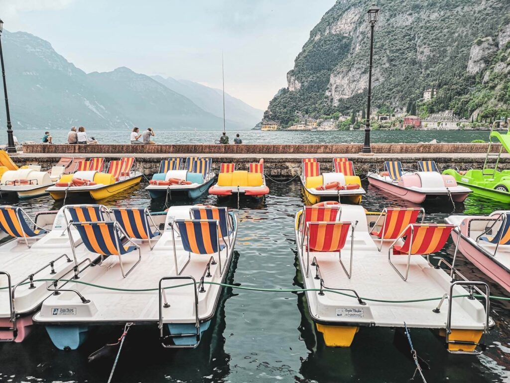 Freizeitaktivitäten in Riva del Garda am nördlichen Gardasee in Italien: Das Bild zeigt bunte Tretboote an der Uferpromenade von Riva del Garda, im Hintergrund sind der Gardassee und die Berge zu sehen