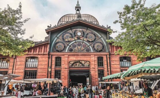 Reisetipps Hamburg: Fischauktionshalle auf dem Hamburger Fischmarkt mit Eingang und Marktständen links und rechts – Blick auf die belebte Marktszene
