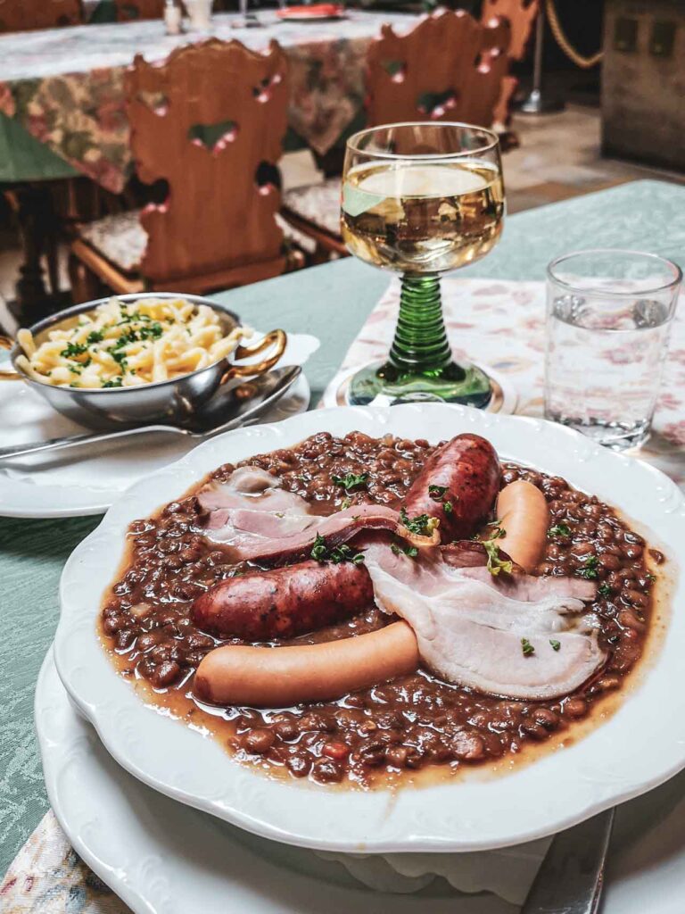 Deftiges Mittagessen im Baumeisterhaus in Rothenburg ob der Tauber: Linseneintopf mit Würstchen und Spätzle, dazu ein Glas Weißwein aus Franken