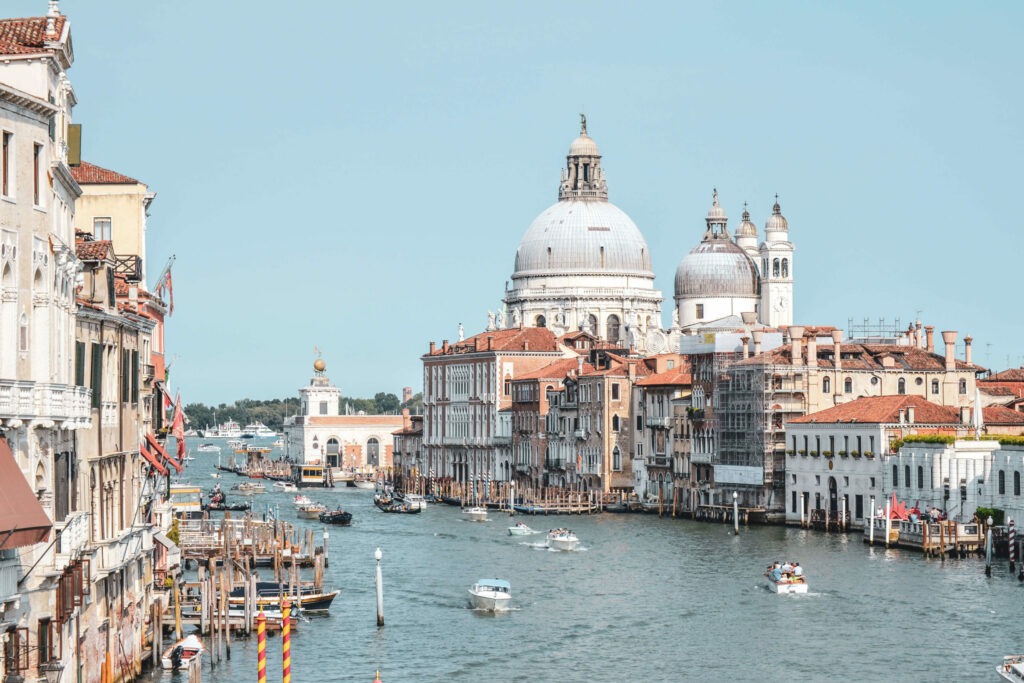 Der Canal Grande in Venedig in Italien im Sommer mit Blick auf die Kirche Santa Maria della Salute, eine barocke Kirche im Sestiere Dorsoduro in Venedig an der Einfahrt zum Canal Grande. Auf dem Kanal sind überall weiße Botte und schwarze Gondeln zu sehen. Links und rechts befinden sich Bootsanlegestellen für die Boote