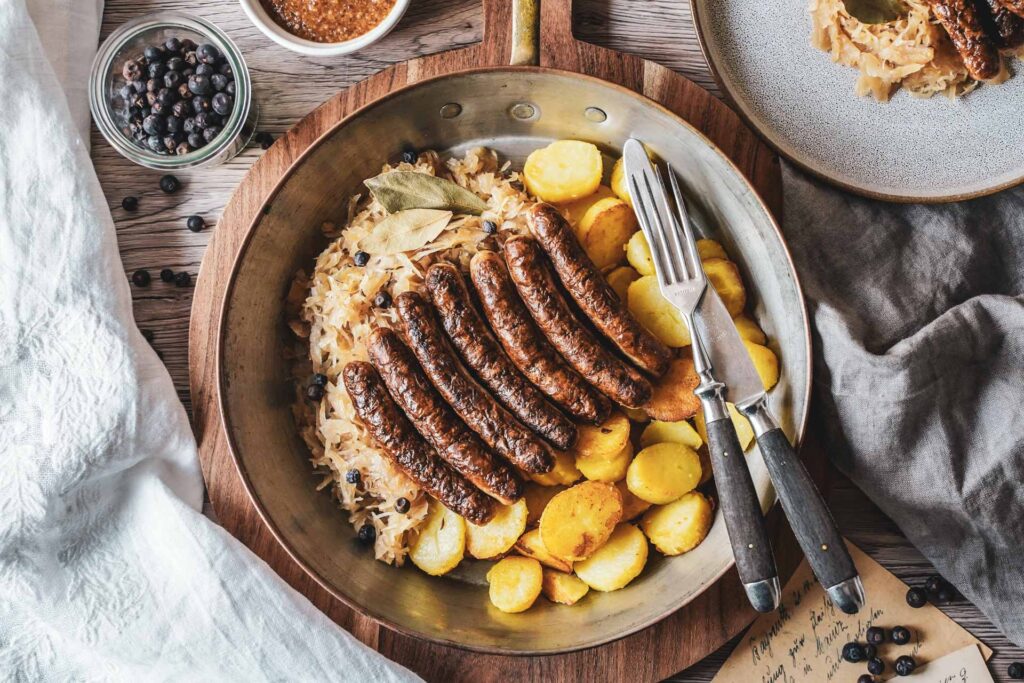 Rostbratwürste mit Sauerkraut und Bratkartoffeln in einer Kupferpfanne serviert