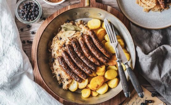 Rostbratwürste mit Sauerkraut und Bratkartoffeln in einer Kupferpfanne serviert