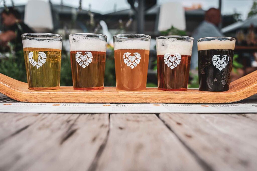 Foodtipps für Bayreuth: Biertasting im Restaurant Liebesbier der Brauerei Maisel mit regionalen und internationalen Bieren der Brauerei Maisel in kleinen Biergläsern auf einem Holzbrett. Auf den Gläsern ist das Logo des Restaurants abgebildet: ein Hopfenherz in Weiß