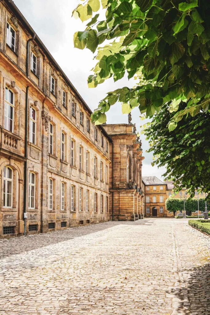 Sehenswürdigkeiten in Bayreuth: Die Vorderseite der Sandsteinfassade des Neuen Schlosses am späten Nachmittag im Frühling mit Bäumen im Vordergrund