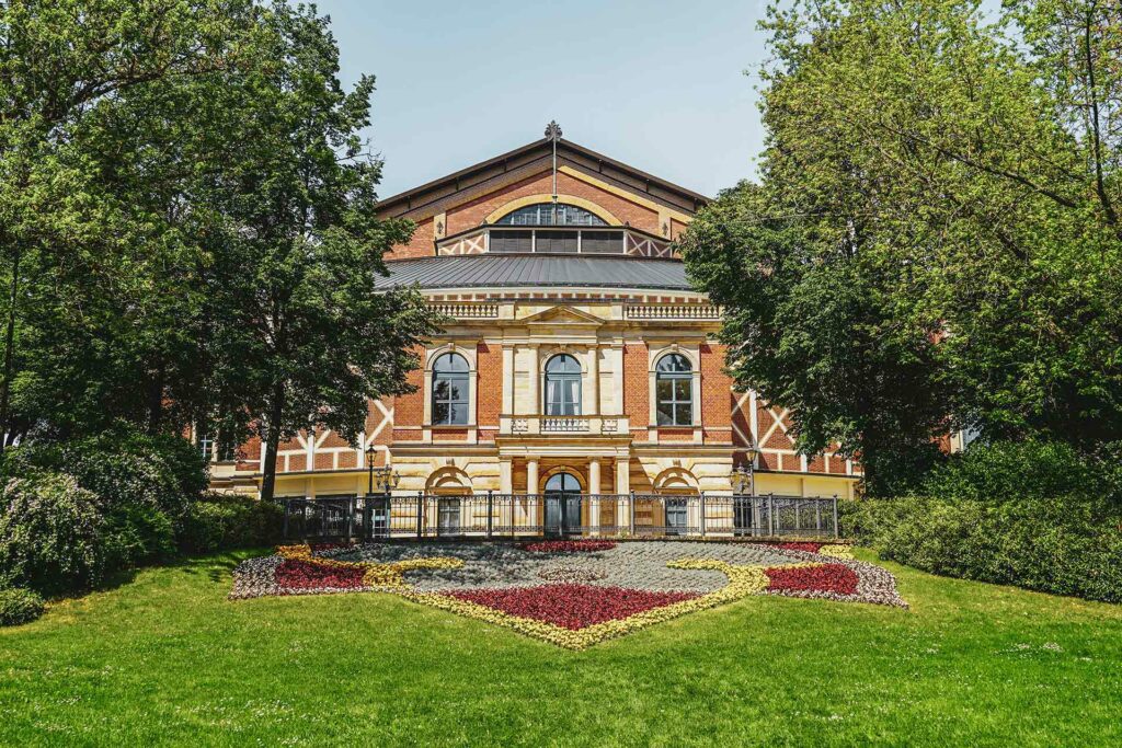 Das Festspielhaus von Richard Wagner auf dem Grünen Hügel in Bayreuth im Sommer. Vor dem Backsteingebäude sind bunte Blumenbeete in Rot und Gelb zu sehen