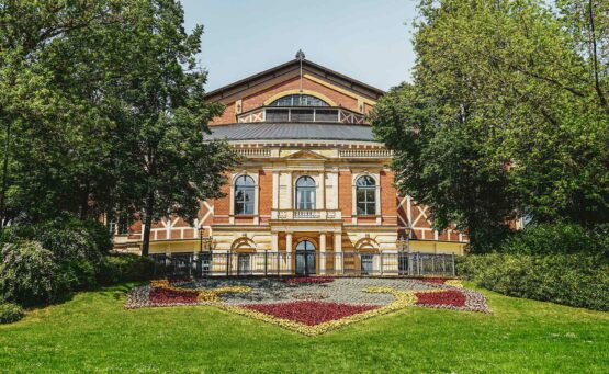 Das Festspielhaus von Richard Wagner auf dem Grünen Hügel in Bayreuth im Sommer. Vor dem Backsteingebäude sind bunte Blumenbeete in Rot und Gelb zu sehen