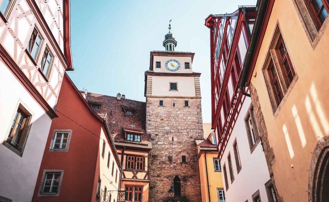 Das mittelalterliche Rothenburg ob der Tauber. Das Bild zeigt das Galgentor, umgeben von Fachwerkhäusern in Rot-, Gelb- und Orangetönen im Abendlicht