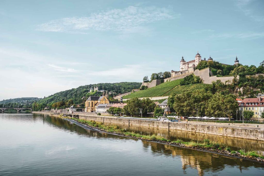 Reisetipps und Sehenswürdigkeiten Würzburg: Blick auf die Festung Marienberg und den Main von der Alten Mainbrücke aus im Sommer bei Sonnenschein und blauem Himmel