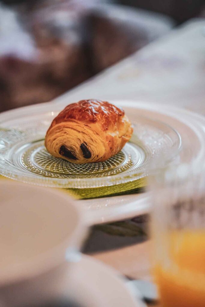 Frühstück im Hotel Oechsle & Brix: Ein kleines Pain au chocloat auf einem Glasteller, im Vordergrund ein Glas mit Orangensaft