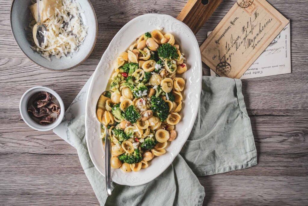 Orecchiette mit Brokkoli, gehobeltem Parmesan und Sardellen auf einer weißen Servierplatte. Authentisches Rezept der apulischen Küche aus Süditalien.