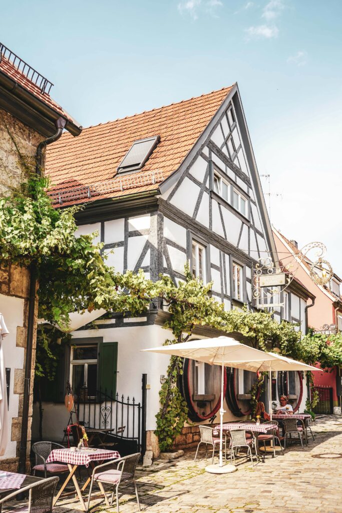 Historisches Fachwerkhaus des Weinhotels Oechsle & Brix in Sommerhausen mit Weinranken und weißen Sonnenschirmen vor dem Haus.