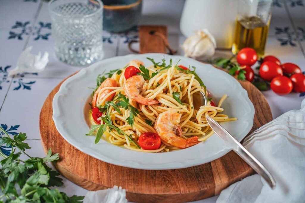Italienisches Pasta-Rezept: Spaghetti mit Garnelen, Kirschtomaten und Rucola auf einem weißen Teller mit Olivenöl, Knoblauch und frischen Zutaten
