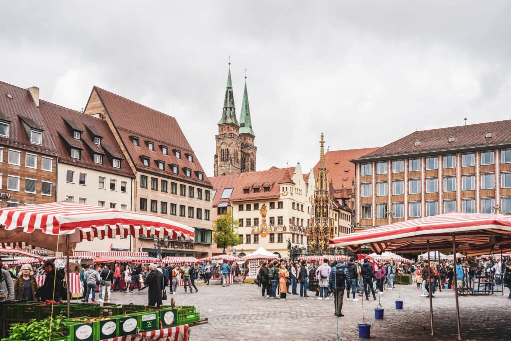 Im Herzen der Stadt: Wochenmarkt auf dem Nürnberger Hauptmarkt mit Marktständen mit rot-weiß gestreiften Planen. Im Hintergrund die Kirche St. Sebald und der Schöne Brunnen