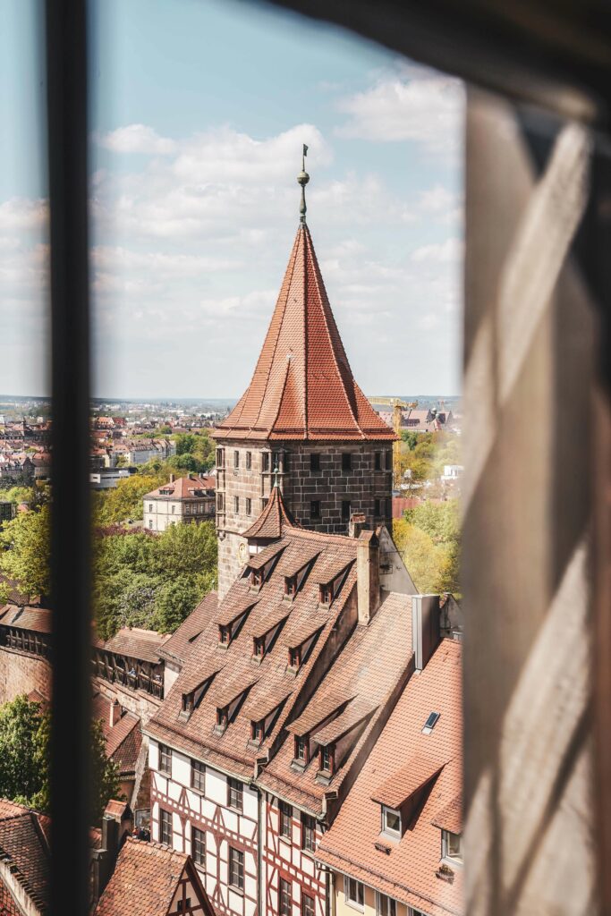 Blick aus einem Fenster der Kaiserburg Nürnberg auf einen Turm und Teil der Stadtmauer mit typischen Fachwerkhäusern
