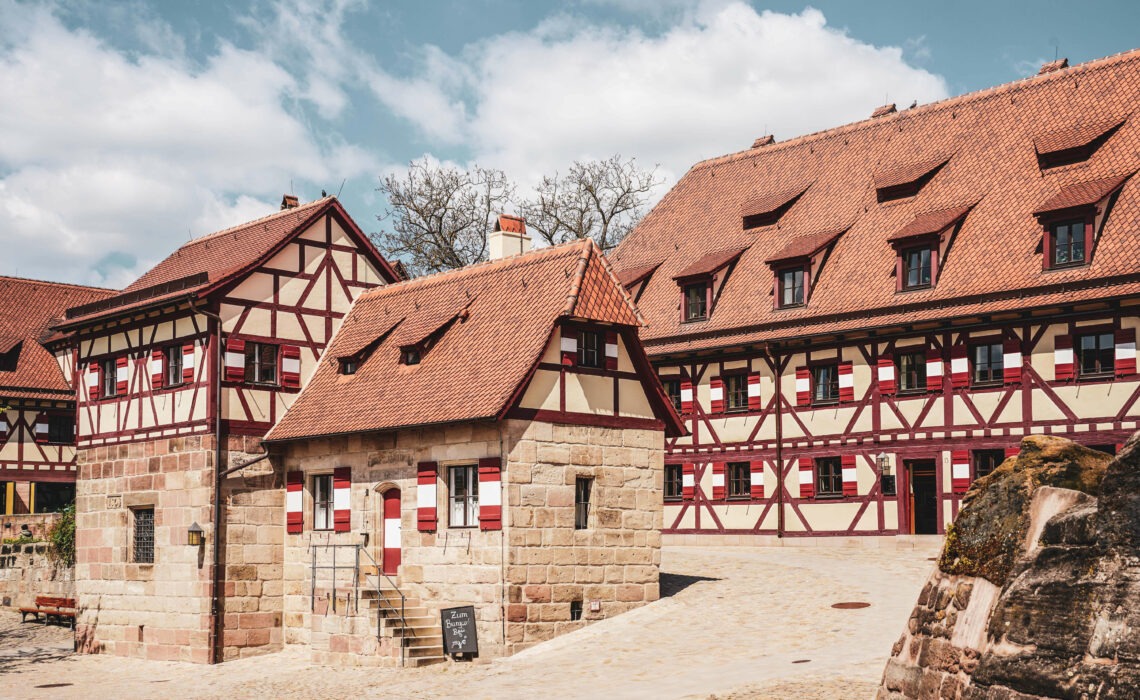 Auf der Kaiserburg Nürnberg: Fachwerkhäuser mit Sandstein und typischen Fensterläden in Rot und Weiß. Im Vordergrund das Brunnenhaus der Kaiserburg.