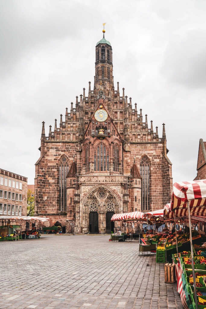 Der Hauptmarkt von Nürnberg mit Blick auf die Frauenkirche. Im Vordergrund sind Obst- und Gemüsestände mit rot-weiß-gestreiften Planen zu sehen.