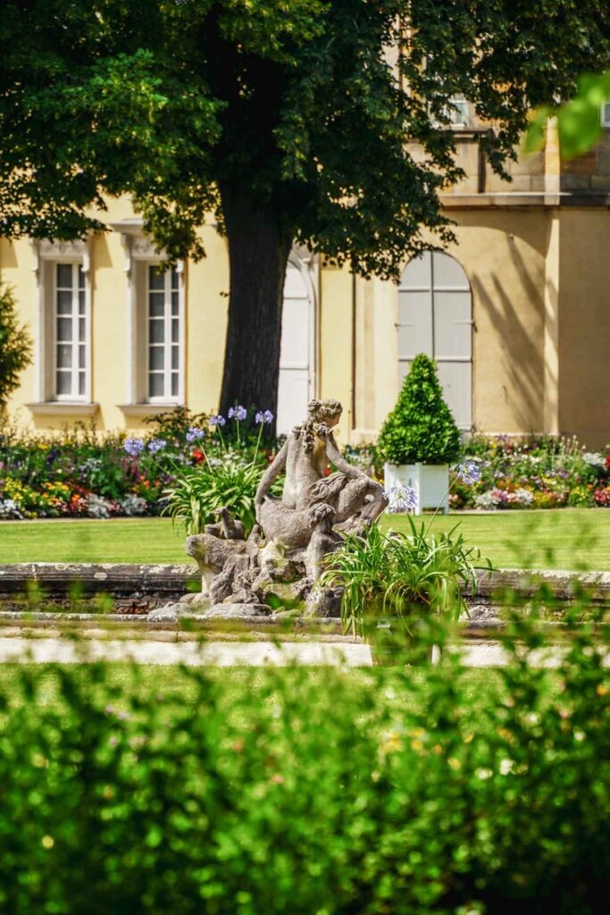 Sehenswürdigkeiten in Bayreuth: Der Hofgarten des Neuen Schlosses. Blick auf das Parterre mit Amphitrite-Brunnen über eine grüne Hecke hinweg