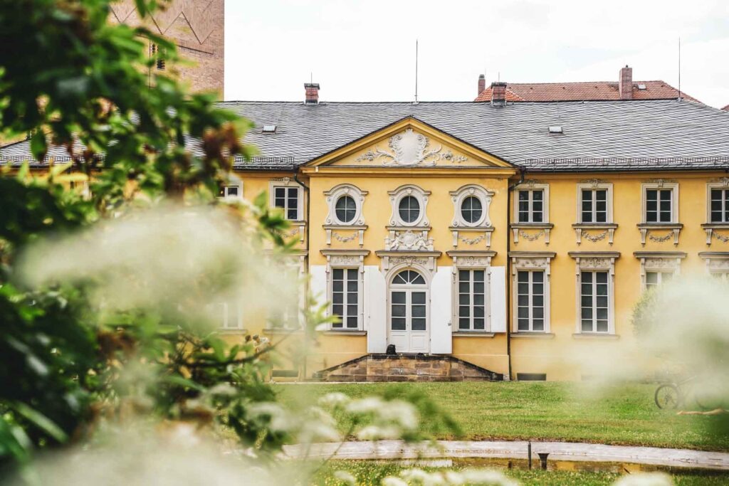 Sehenswürdigkeiten in Bayreuth: Der Blick auf das Italienische Schlösschen des Neuen Schlosses vom Hofgarten aus durch weiße Blumen hindurch