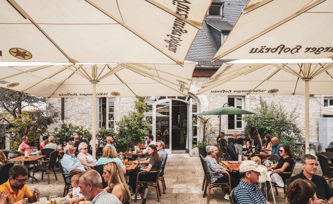 Foodtipps Würzburg: Die voll besetze Terrasse des Brauereigasthofs Alter Kranen in mit weißen Sonnenschirmen