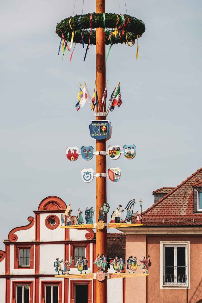 Reisetipps Würzburg: Der Maibaum auf dem Marktplatz in Würzburg mit bunten Zunftschildern und Zunftwappen der traditionellen Handwerksberufe
