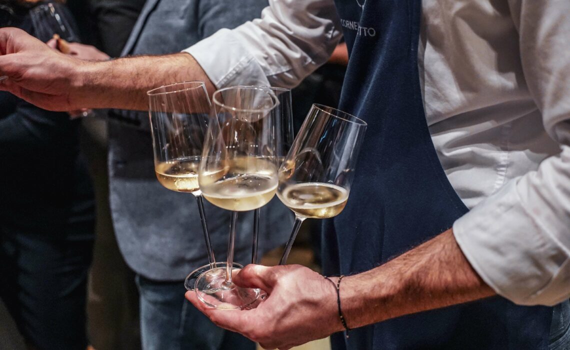 Piper-Heidsieck Champagner Blanc de Noirs »Essentiel« in Gläsern, deie vom Servicepersonal der Cucina Cornelia Poletto in marineblauen Schürzen und weißen Hemden gereicht werden