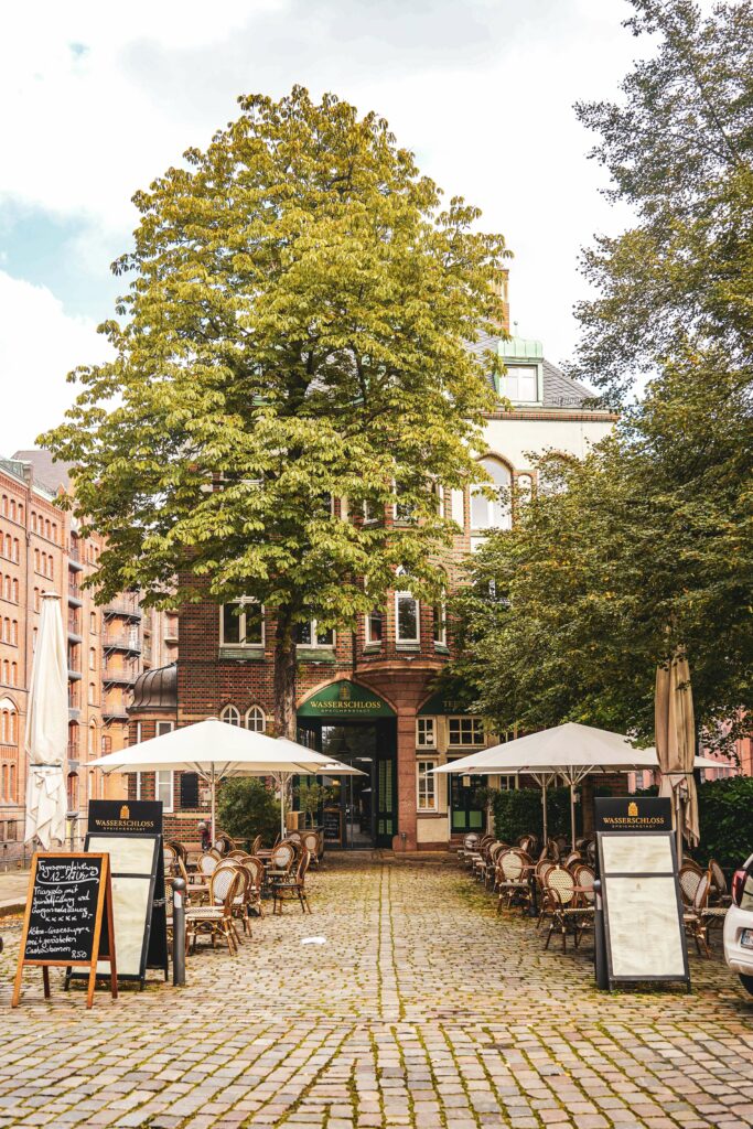 Fotospots in Hamburg im Herbst: Das Wasserschloss vom Holländischbrookfleet aus mit Herbstbäumen und weißen Sonnenschirmen m Vordergrund in der Hamburger Speicherstadt