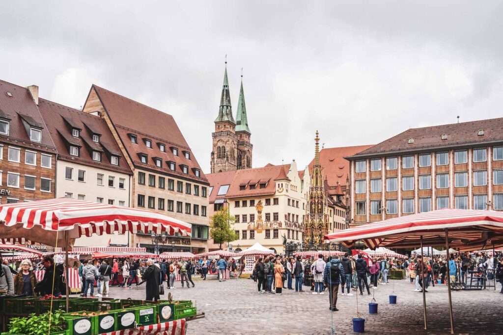 Reisetipps Nürnberg: Im Herzen der Stadt: Wochenmarkt auf dem Nürnberger Hauptmarkt mit Marktständen mit rot-weiß gestreiften Planen. Im Hintergrund die Kirche St. Sebald und der Schöne Brunnen