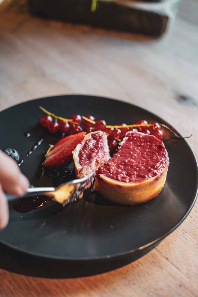Foodtipps Nürnberg: Veganer Cheesecake im Café-Restaurant ZEIT & RAUM auf schwarzem Teller mit roten Johannisbeeren dekoriert
