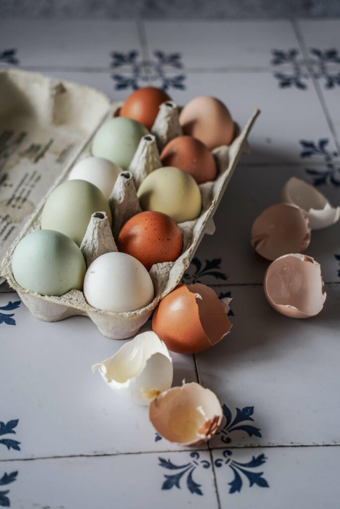 Bunte Eier zu Ostern in Pastellgrün und Pastellblau vom Bauernhof – ganz ohne Bemalen! Für den saftigen Karottenkuchen haben wir ein paar aus der Eierschachtel genommen, die Schalen liegen daneben auf den weißen Fliesen mit klassischem dunkelblauen Muster.