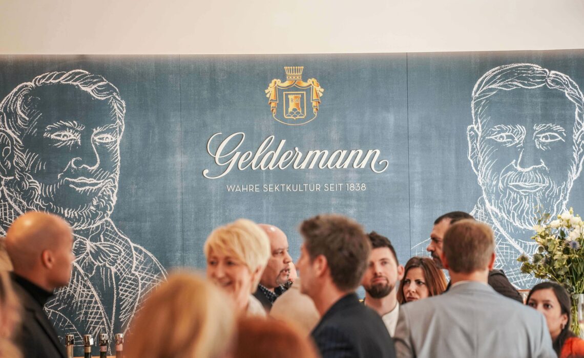 Launch Event zur Geldermann Grande Réserve Cuvée in der Geldermann-Boutique in Breisach am Rhein mit Pressevertretern aus ganz Deutschland vor der hellblauen Logo-Wand mit Geldermann-Logo