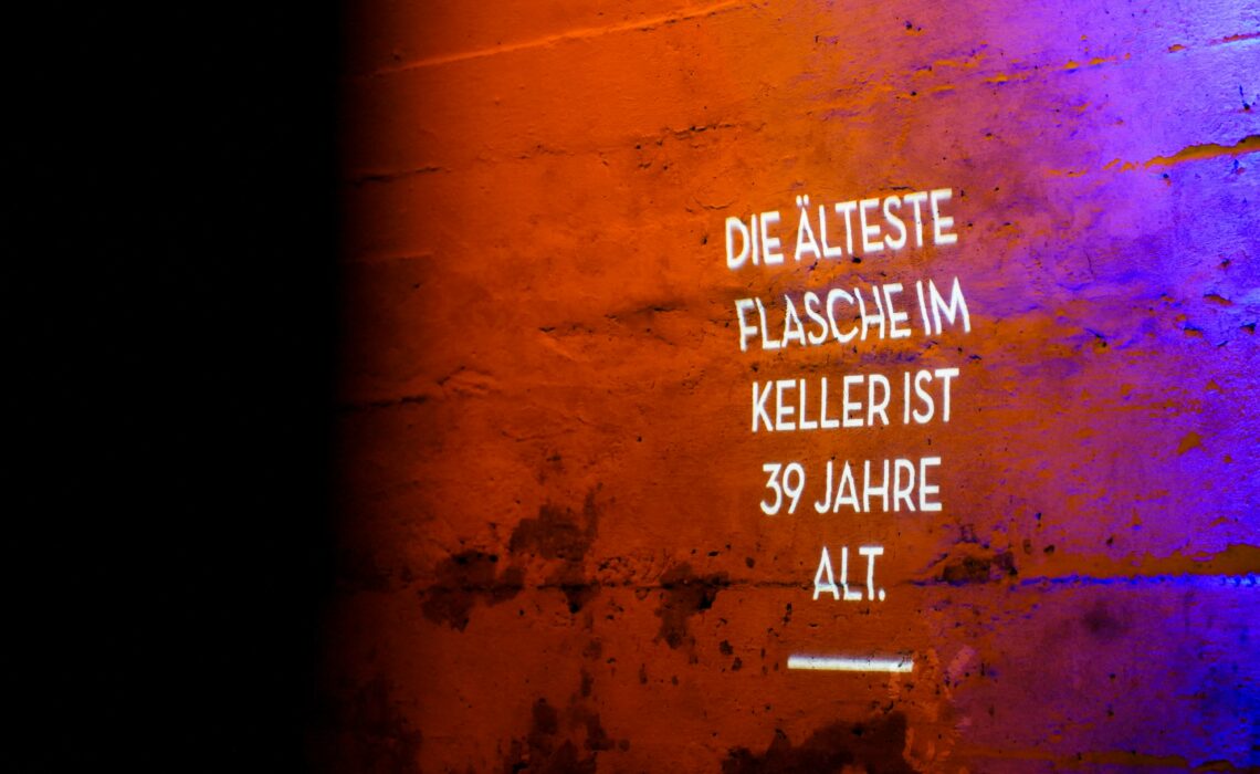Führung im historischen Sektkeller der Geldermann-Privatsektkellerei in Breisach: Wand mit Infotext in Weiß: Die Älteste Flasche im Keller ist 39 alt.