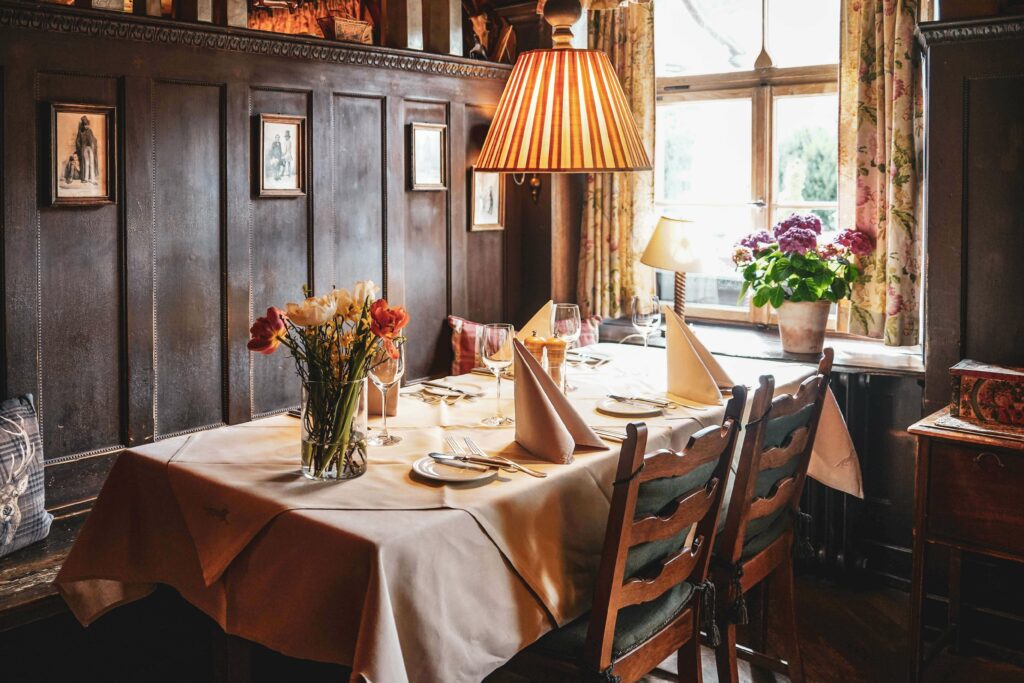 Die einladende Alte Stube im Restaurant des Romantik-Hotels Spielweg im Schwarzwald mit traditioneller Holzvertäfelung. Auf dem gedeckten Tisch stehen frische Frühlingsblumen und durch die Fenster bricht das Sonnenlicht herein