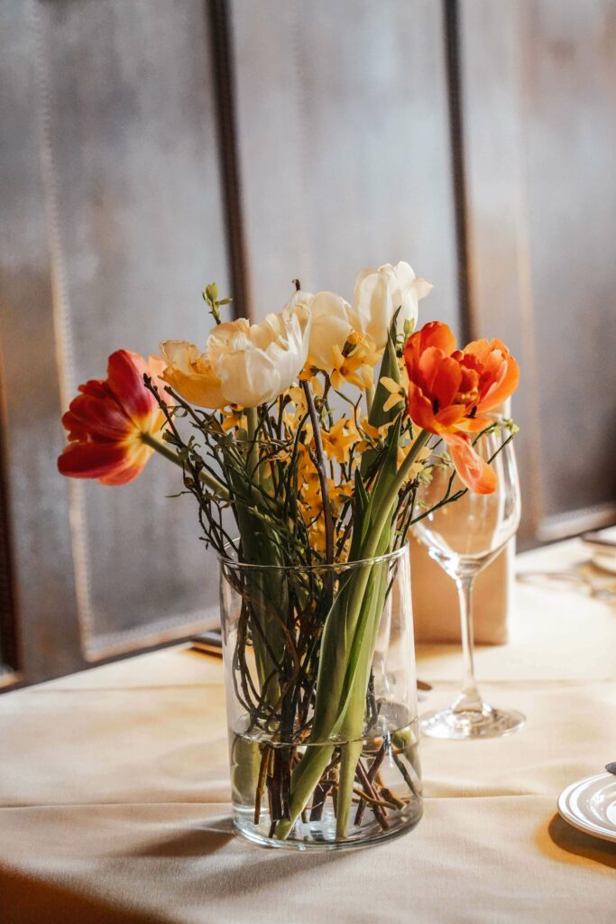 Frische Frühlingsblumen in Rot, Weiß und Gelb auf einem gedeckten Tisch in der Alten Stube des Restaurants Spielweg. Im Hintergrund ist die traditionelle Holzvertäfelung zu sehen