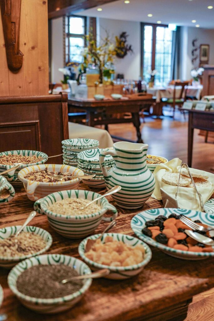 Das Frühstücksbuffet im Romantik-Hotel wird serviert in traditionellen Schalen aus Gmund-Keramik mit grünem Muster. Auf dem Tusch stehen Schalen mit Müsli, Kernen, getrockneten Früchten und getrocknetem Obst