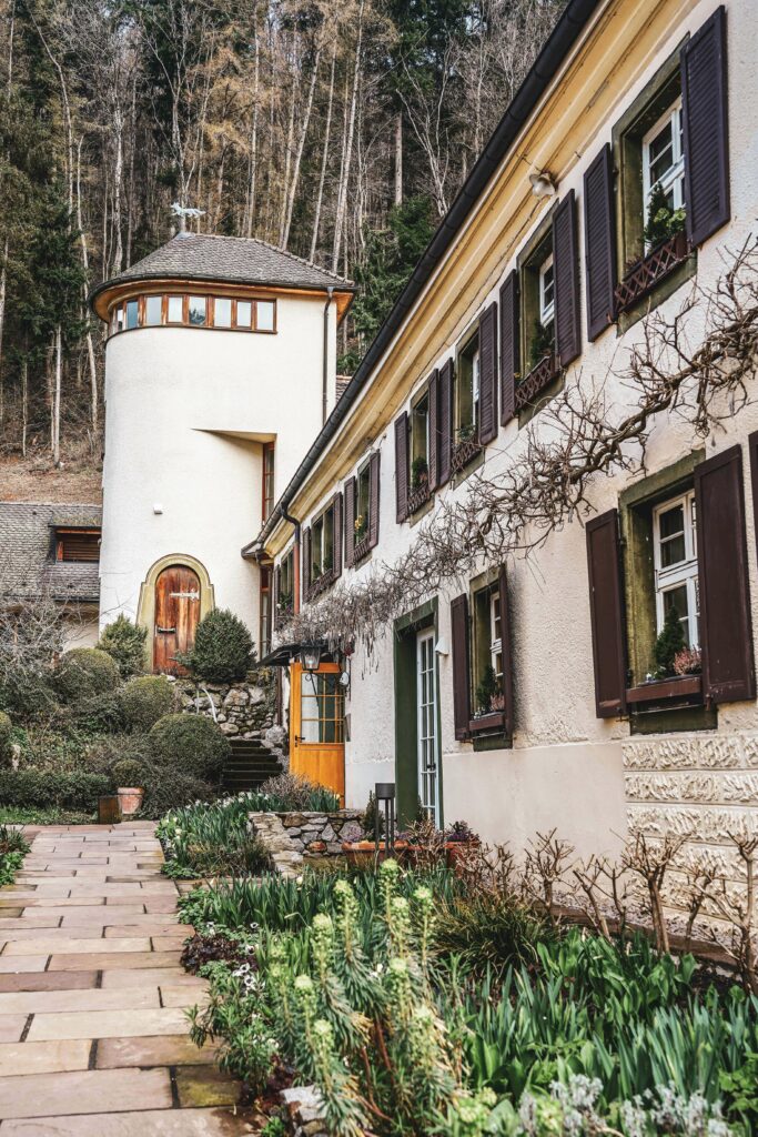 Das Stammhaus des Romantik-Hotels Spielweg im Münstertal im Schwarzwald mit einem Türmchen und Blumenbeeten entlang des Weges