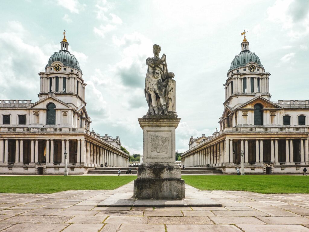 Geheimtipps für Sehenswürdigkeiten in London: Das Old Royal Naval College in Greenwich mit imposanten Türmen und Säulen. In der Mitte befindet sich eine Statue von König George III.