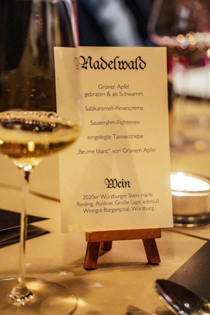 Das kleine Menü-Schild auf der Mini-Staffelei auf dem Tisch im Sterne-Restaurant KUNO 1408 in Würzburg kündigt das Dessert „Nadelwald“ an