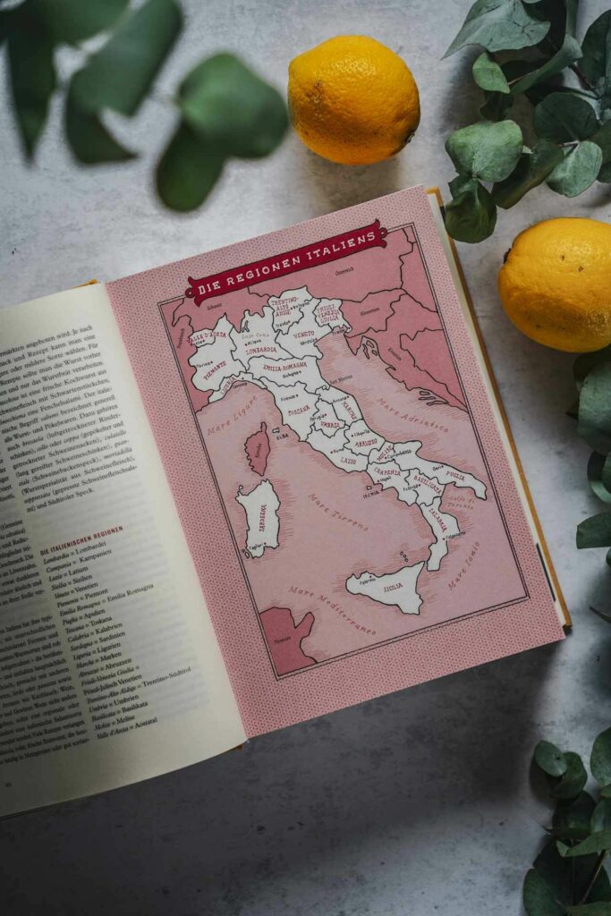 Das Italien-Kochbuch La Cucina der Accademia italiana della cucina aus dem Callwey-Verlag. Das Bild zeigt das aufgeschlagene Buch mit einer illustrierten Karte aller Regionen Italiens, umgeben von Eukalyptus-Blättern und Zitronen
