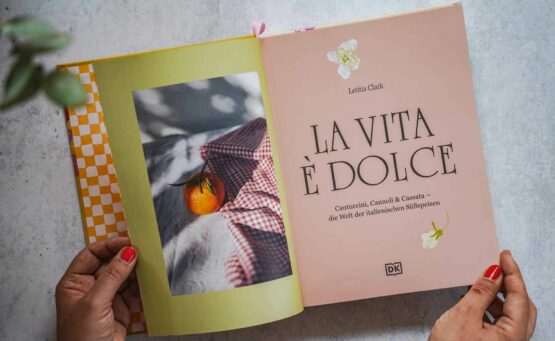 Die schönsten Kochbücher für den Sommer: Das Italien-Kochbuch La vita è dolce aus dem DK-Verlag. Das Bild zeigt den Innentitel auf Pastellfarbenem Hintergrund und einem Foto, das eine Orange neben einem Rot-Weiß karierten Küchentuch zeigt, Eukalyptus-Blättern