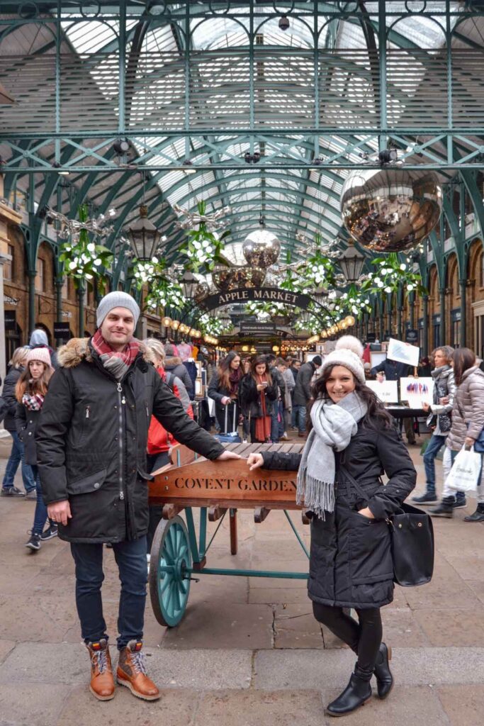 Blogger Alex und Flo in der Markthalle von Covent Garden vor einem typischen geschmückten Blumenwagen. Der Apple Market ist mit großen silbernen Weihnachtskugeln und Mistelzweigen geschmückt