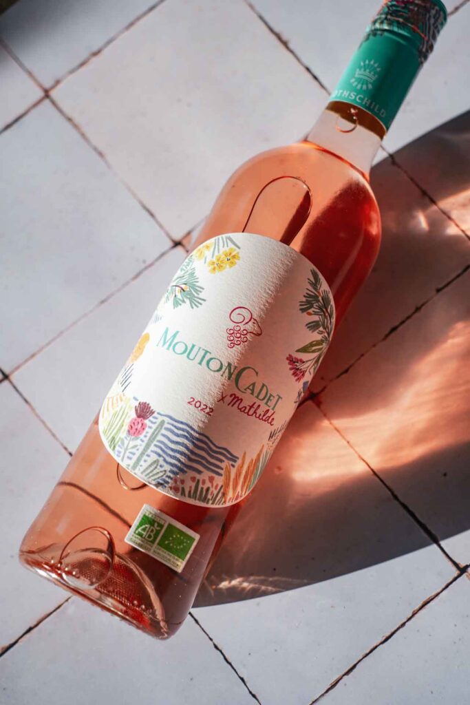 Wein-Empfehlung: Der Roséwein Mouton Cadet x Mathilde Rosé Bio des Weinguts Baron Philippe de Rothschild aus Bordeaux in Frankreich. Das Bild zeigt die Flasche mit sommerlichem Etikett mit Illustrationen in Türkis und Pink