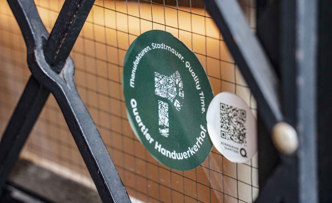 Eröffnung der Genussecke in der Tourist Info im Handwerkerhof Nürnberg . Quartiers-Logo des Handwerkerhof-Viertels als Aufkleber im Schaufenster in Dunkelgrün mit einer stilisierten weißen Axt