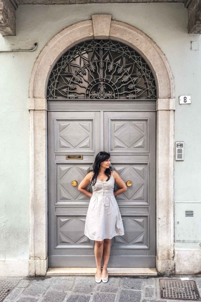Die schönsten Orte am Gardasee: Alexandra vor einer grauen Altbau-Tür in Desenzano del Garda mit hellgrauem Sommerkleid