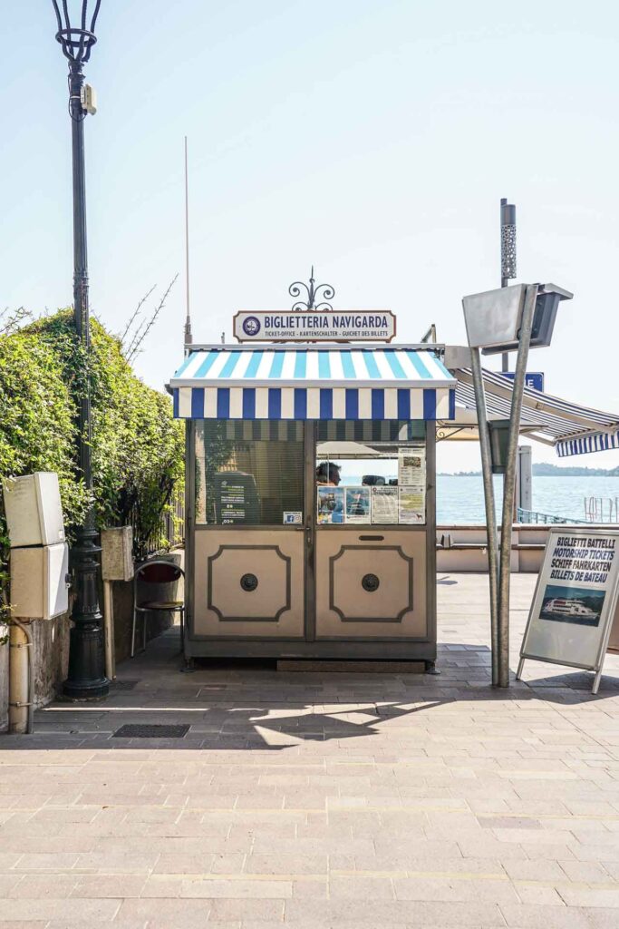 Die schönsten Orte am Gardasee: Ticket Office an der Schiffsanlegestelle in Gardone Riviera mit Blau-Weiß-gestreiften Markisen