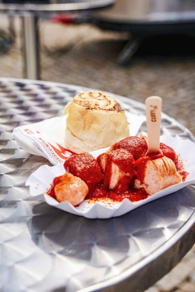 Geldermann x KPM –Launch der Bayreuther Festspiel-Cuvée zu Richard Wagners Die Meistersinger von Nürnberg 2025: Currywurst von Curry 36 mit Brötchen und Holzspieß beim Sektempfang im Innenhof der KPM Berlin