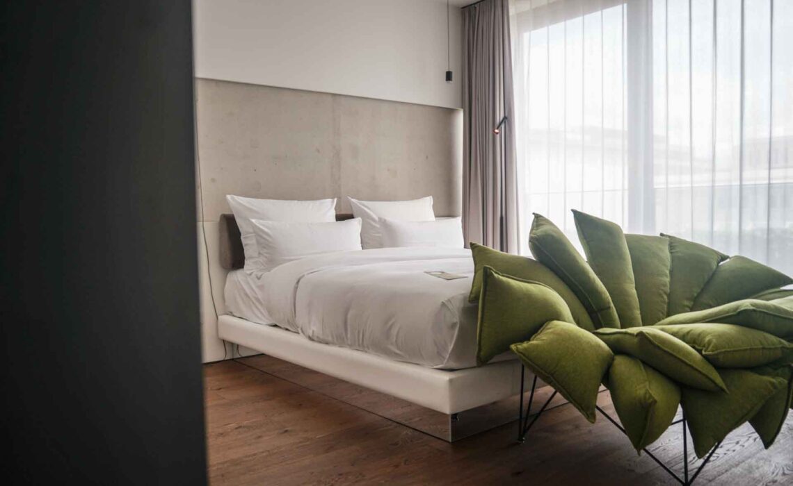Geldermann x KPM –Launch der Bayreuther Festspiel-Cuvée zu Richard Wagners Die Meistersinger von Nürnberg 2025: Design-Zimmer im KPM Hotel & Residences mit weißem Bett und grünem Designersessel vor großen Fenstern
