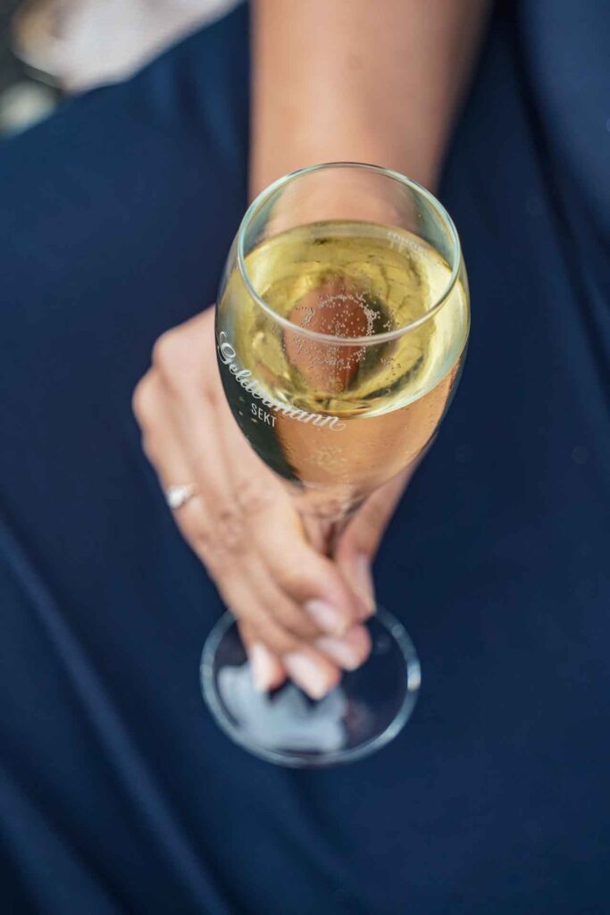Mit Geldermann bei den Bayreuther Festspielen 2025: Content Creatorin Alexandra Baier hält ein Glas der Geldermann Bayreuther Sekt-Cuvée in der Hand vor ihrem dunkelblauen Abendkleid